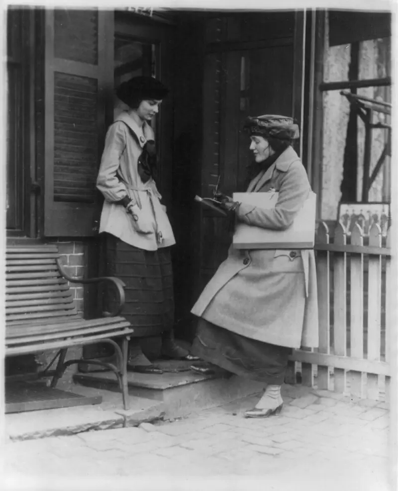 Woman taking census of another woman at door of house.
